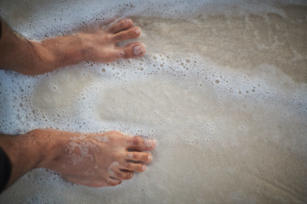 HIGH ANGLE VIEW OF HAND TOUCHING WATER ON WET SAND