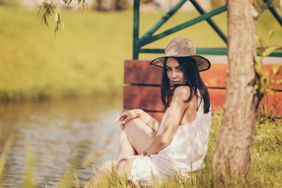 Portrait of young woman sitting at the shade of a tree by lake