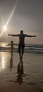 Men standing on beach against sky during sunset