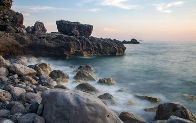 Rocks on beach against sky during sunset