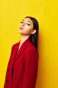 Portrait of young woman standing against yellow background