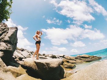 Man standing on rock by sea against sky