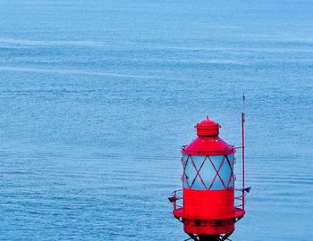 Red lighthouse in sea against blue sky