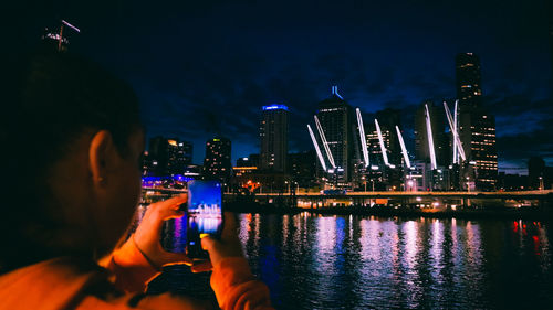 People photographing illuminated modern buildings in city at night