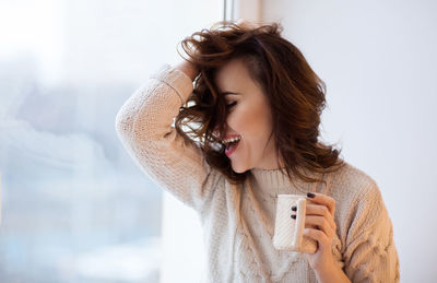 Cheerful woman holding coffee cup at home