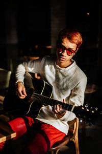 Young man playing guitar while sitting on chair