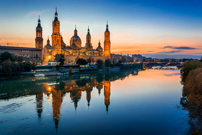 Reflection of illuminated building in river against sky during sunset