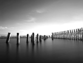 Wooden posts in sea against sky in city