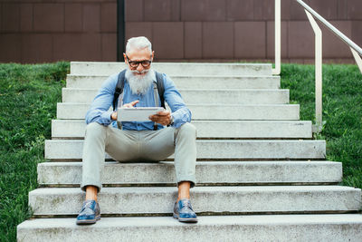 Full length of man using mobile phone while sitting on staircase