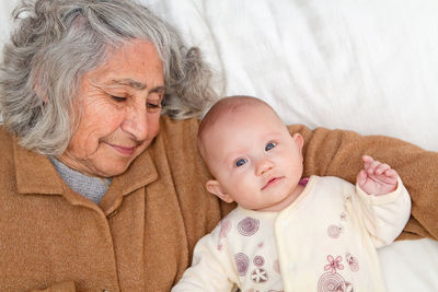 Portrait of baby girl lying by grandmother sleeping on bed at home