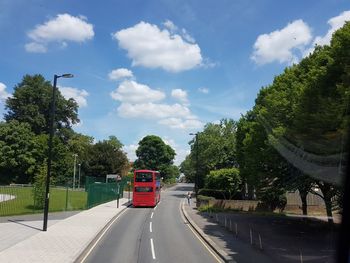 Road amidst trees against sky in city of london with red london bus