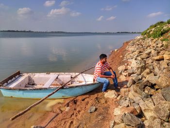 Side view of boy in boat on shore against sky
