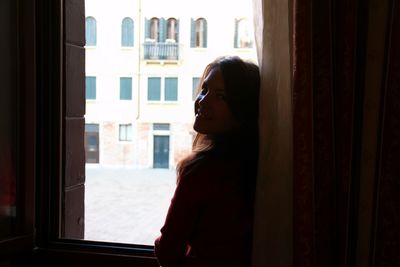 Portrait of smiling woman standing by window at home