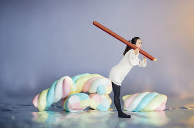 Digital composite image of woman holding chocolate stick while standing by marshmallow against wall