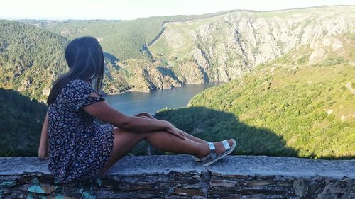 Woman sitting by lake against mountain