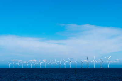 Wind turbines by sea against sky