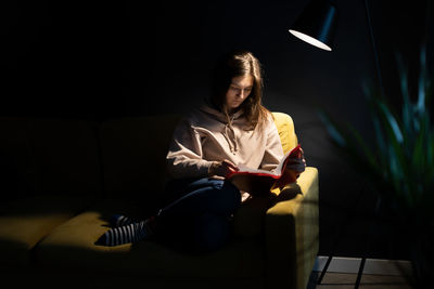 Full length of young woman reading book sitting on sofa