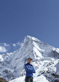 Low angle portrait of young man standing against snowcapped mountains