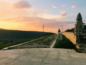 Footpath by road against sky during sunset
