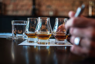 Close-up of hand holding pen against scotch whiskey in glasses at table