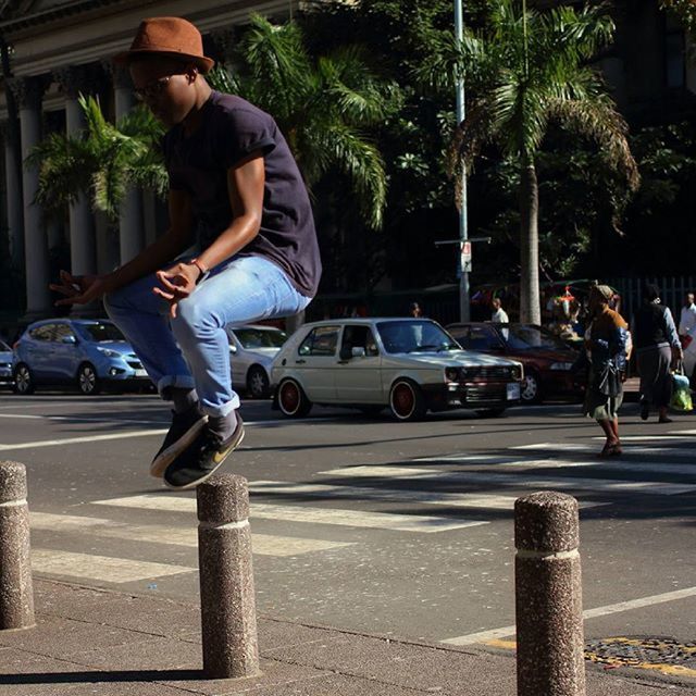 lifestyles, leisure activity, full length, tree, casual clothing, street, transportation, men, road, land vehicle, city, mode of transport, car, building exterior, motion, sunlight, city life, young adult