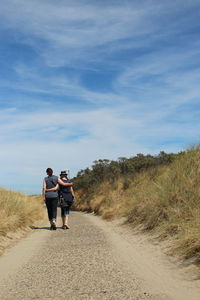 Rear view of men walking on road against sky