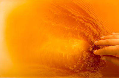 Close-up of hand in orange liquid