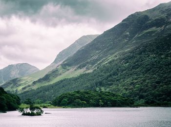 Small island with trees on a lake with mountains towing above it 