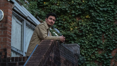 Low angle view of young man standing by retaining wall