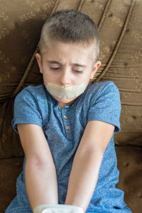 Boy with adhesive tape on mouth sitting on sofa