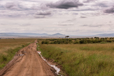 Empty road amidst field against sky