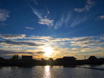 Silhouette buildings by river against sky during sunset