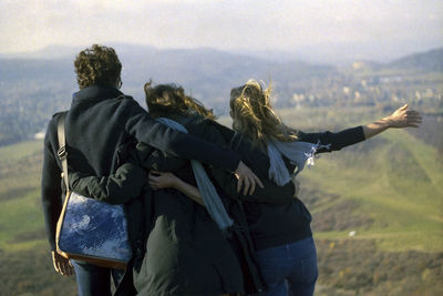 Rear view of friends standing on field against sky