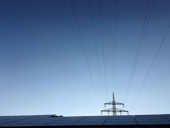 Low angle view of solar panels by electricity pylon against clear blue sky