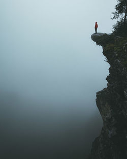 Man standing on cliff during foggy weather against sky