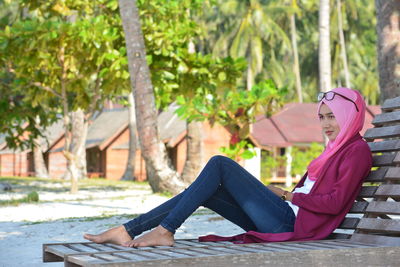 Side view of beautiful woman sitting on wooden deck chair at beach