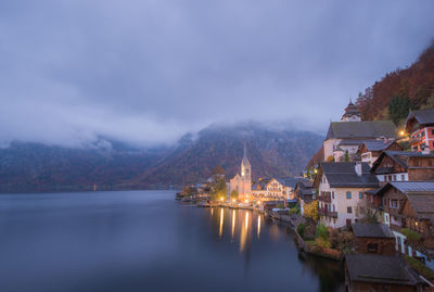 Illuminated buildings by mountains against sky at dusk