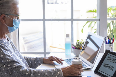 Side view of senior wearing mask working at home