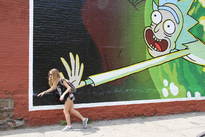 Full length of young woman standing against brick wall