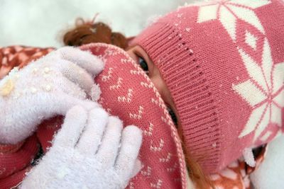 High angle portrait of girl covering face while lying on snow