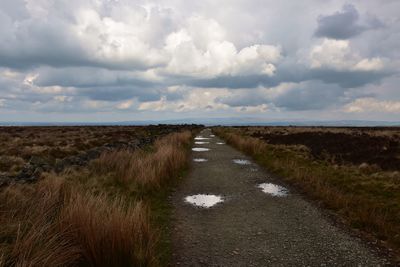 View down track over moorland after rain against cloudy sky