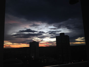 Silhouette buildings against dramatic sky during sunset