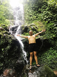 Full length of shirtless man standing on rock in forest