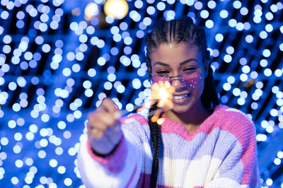 Cheerful black woman with braided hairstyle and pink glasses enjoying christmas lights