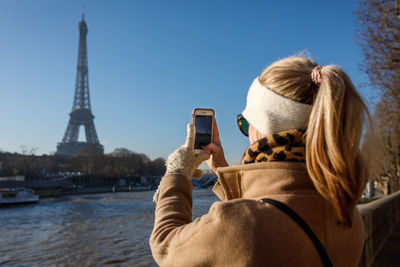 A young adult takes an iphone picture of the eiffel tower in paris.