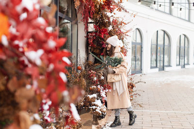 A stylish young woman with branches of nobilis looks into the windows of christmas shops