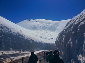 People on snowcapped mountain against blue sky