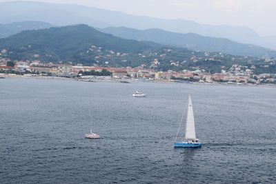 Sailboat sailing on sea by city against sky