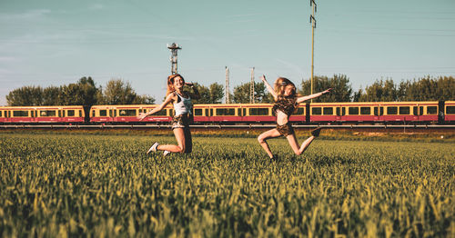 Friends jumping on grassy field against sky