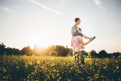 Side view of woman standing on field against sky during sunset